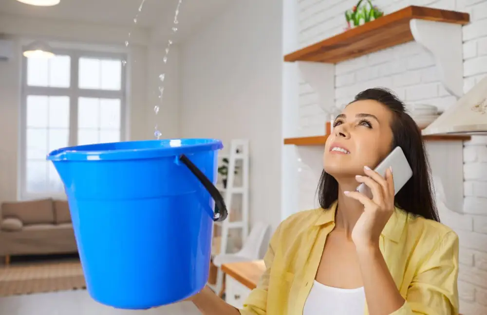 Woman holding a bucket to catch the water leaking from the roof